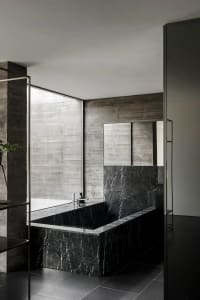 Modern minimalist bathroom with black marble tub and concrete walls.