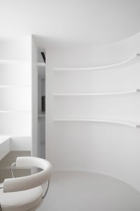 A minimalist white interior design space featuring a circular table and a white chair.
