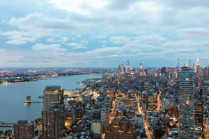 New York City skyline at dusk, featuring high-rise buildings and a river.
