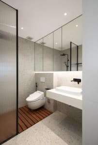 Modern minimalist bathroom with white fixtures, terrazzo floor, and large mirror.