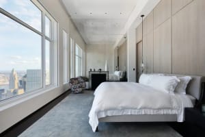 Modern minimalist bedroom with a large window, white bedding, and a floral armchair.