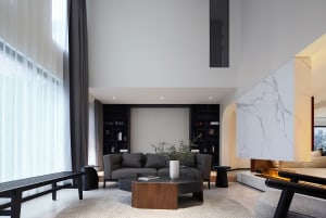 A modern living room featuring stone marble finishes, dark grey upholstered furniture, a low wooden coffee table, and floor-t
