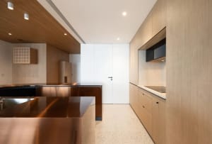 A modern residential kitchen with wooden cabinets and flooring, featuring sleek countertops and a minimalist design.