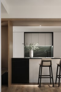 Modern minimalist kitchen with marble backsplash, bar stools, and sleek white cabinets.