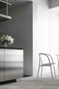 Modern kitchen with sleek steel cabinets and glass interior, featuring white lilies in a vase.
