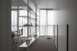 A minimalist office interior with glass shelving, a desk, and a chair.