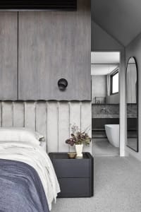 A modern bedroom featuring a gray wall with a textured pattern, a bed with white bedding, and a dark nightstand with a plant.