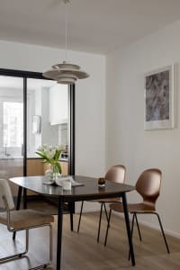 A modern dining room with a wooden table and chairs, white tulips in a vase, and a geometric pendant light hanging from the c