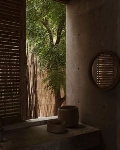 A minimalist bathroom featuring concrete walls and floor, with natural light filtering through a window surrounded by green f
