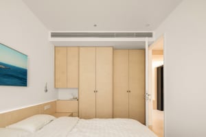 A minimalist bedroom featuring wood cabinets and a bed with white sheets and pillows.