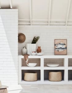 A minimalist indoor space featuring white brick and concrete shelves with various decorative objects and storage baskets.
