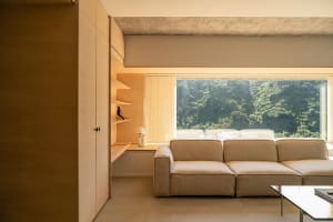 A modern living room with a compact design, featuring a beige sectional sofa, wooden shelves, and a glass coffee table with a