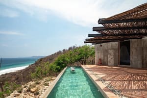 Modern minimalist residential building with a concrete and wood exterior featuring a small rectangular pool with clear water 