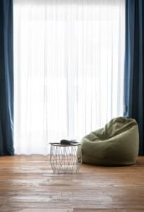 Modern living room featuring a green bean bag chair, a wooden side table with a book, and large windows with sheer curtains, 