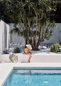 A modern residential patio featuring a concrete pool and surrounding landscaping with concrete retaining walls, palm trees, a
