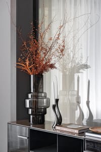 A modern shelf decorated with a tall black vase containing dried flowers, a black bottle, and books.