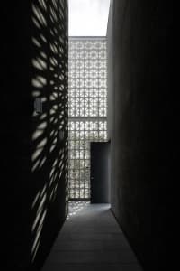 A corridor with concrete walls displaying geometric shadows created by a grid-like structure above.