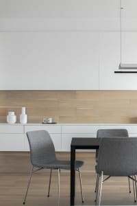A modern dining room featuring a black table, grey upholstered chairs, and a wooden wall with white floating shelves.
