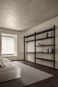 Modern living room with concrete walls, metal shelving, and a plush off-white couch on a gray rug.