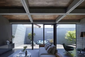 A modern concrete living room featuring a cozy sofa, stylish furniture, and large windows overlooking a serene courtyard.