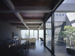 A modern living and dining space with concrete flooring, large windows, and modern lighting fixtures.