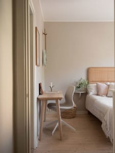 A minimalist bedroom with wooden furniture, a woven headboard bed, and a small wooden desk with a chair, a candle holder, and