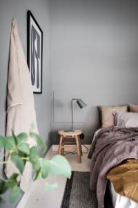 A minimalist bedroom with light grey walls, a wooden stool as a bedside table, and neutral bedding and textiles.