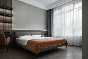 A contemporary minimalist bedroom with a bed dressed in brown blankets and a white bedspread, featuring woven curtains, woode