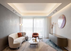 A minimalist living room featuring a curved white sofa with an orange pillow and a side table with books.