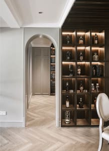A modern bar with wooden shelves displaying various bottles and a decorative hourglass.