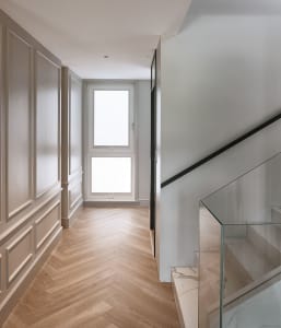 A modern staircase hallway featuring wooden flooring and glass railings.