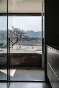 Modern industrial-style bathroom with concrete finishes and a view of mountains and a river through a large window.