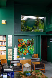 A modern living room with green painted walls, concrete materials, and a variety of plants.