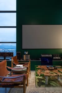 A modern living room with leather chairs, a coffee table, and a large screen on a green wall, featuring concrete flooring and