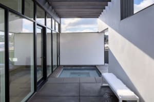 Modern minimalist outdoor space featuring a concrete patio with glass walls and metal furniture.