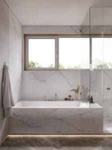 Modern bathroom with marble walls and floor, featuring a bathtub and window.