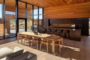 A modern residential kitchen with wooden flooring, cabinetry, and a large dining table.