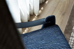 A close-up of a blue textured cloth leather chair with a wooden floor and a white curtain in the background.
