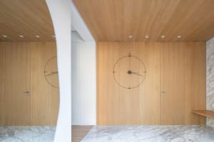 A modern wooden door with a large circular clock embedded in it, situated in a minimalist interior space with white walls and