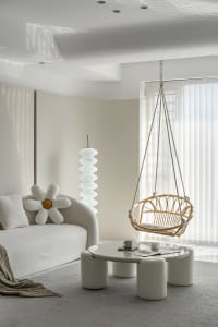 A minimalist interior design featuring a white concrete floor, wool sofa, glass lamp, and rattan hanging chair.