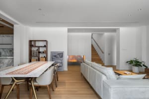 Modern dining room with white marble table and chairs, featuring a cozy fireplace and sleek white couch, surrounded by minima
