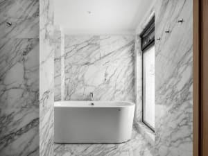 Modern bathroom with marble walls and floor, featuring a freestanding bathtub and a window.