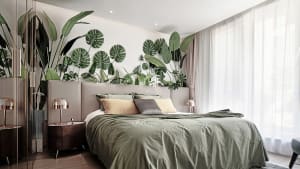 A bedroom featuring a modern bed with green bedding and a wall adorned with plant leaves.