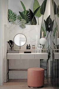 A modern vanity table with a round mirror, marble top, and pink stool.
