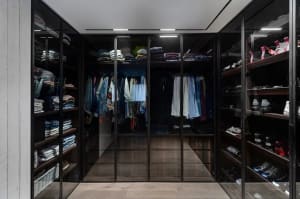 Modern closet with wooden shelves and glass doors displaying neatly arranged clothing and shoes.