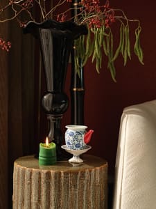 A ceramic teapot with red spout, blue floral pattern, and white base and saucer, placed on a textured wooden table with a gre