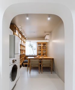 A modern kitchen area with a dining table and chairs, a bookshelf, and a laundry area featuring a washing machine and dryer.