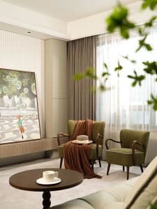 A modern living room with green armchairs, a round wooden table, and a large window covered with sheer curtains and a beige c