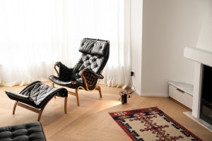 Minimalist living room featuring a leather chair, ottoman, and rug on a wooden floor.