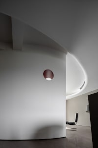 Modern, minimalist room with a sleek, curved concrete wall and a single steel frame chair.